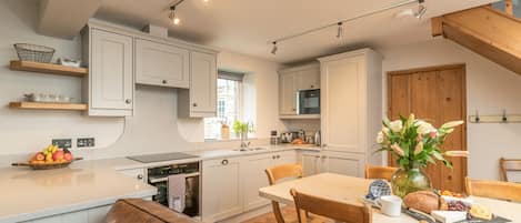 Una cocina moderna con muebles blancos, un comedor con mesa y sillas de madera, y una viga de techo de madera.