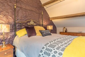 Ein Schlafzimmer mit schrägen Wänden, einem Bett mit gemusterten Betttextilien und einem Kopfende mit dekorativer Gestaltung.