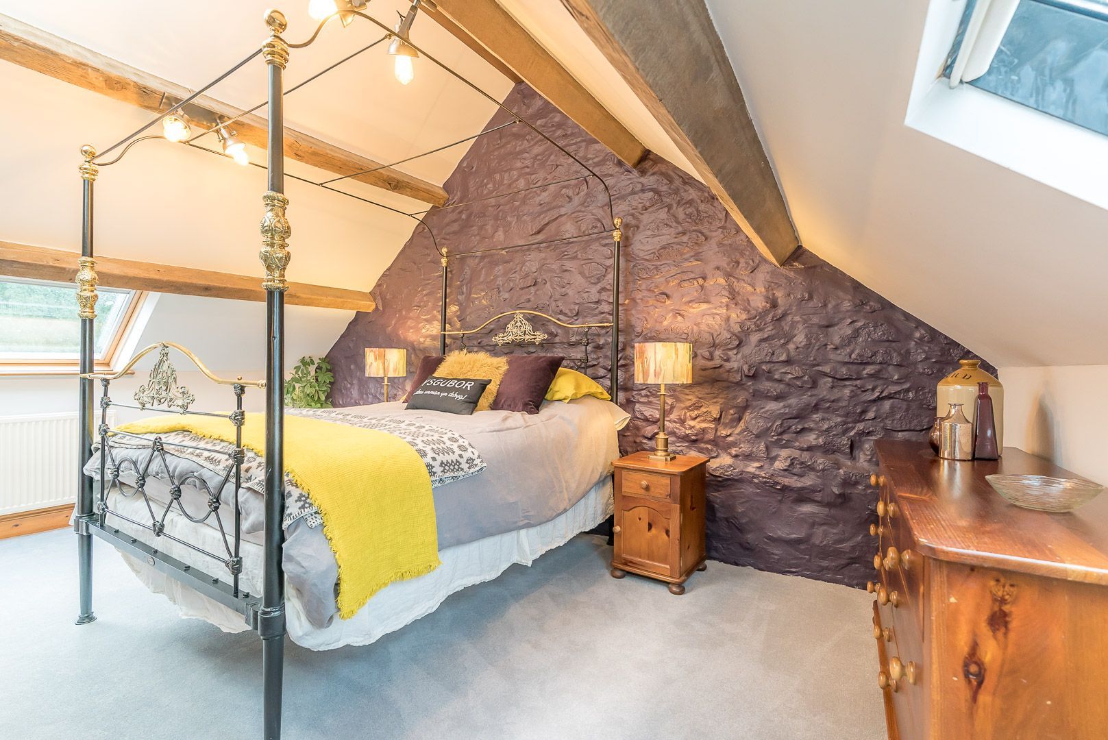 A bedroom with a four-poster bed, a stone accent wall, a nightstand, and a window with a view.