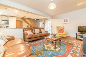 A living room with a brown leather sofa, a yellow armchair, a coffee table, and a colorful rug. - Holiday Cottage On A Working Farm On The Llŷn Peninsula | Ysgubor-Sarn (Pwllheli)