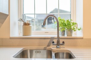 Eine Küchenspüle mit einem modernen Wasserhahn, ein Fenster mit Ausblick und ein Blumentopf am Fensterbrett.