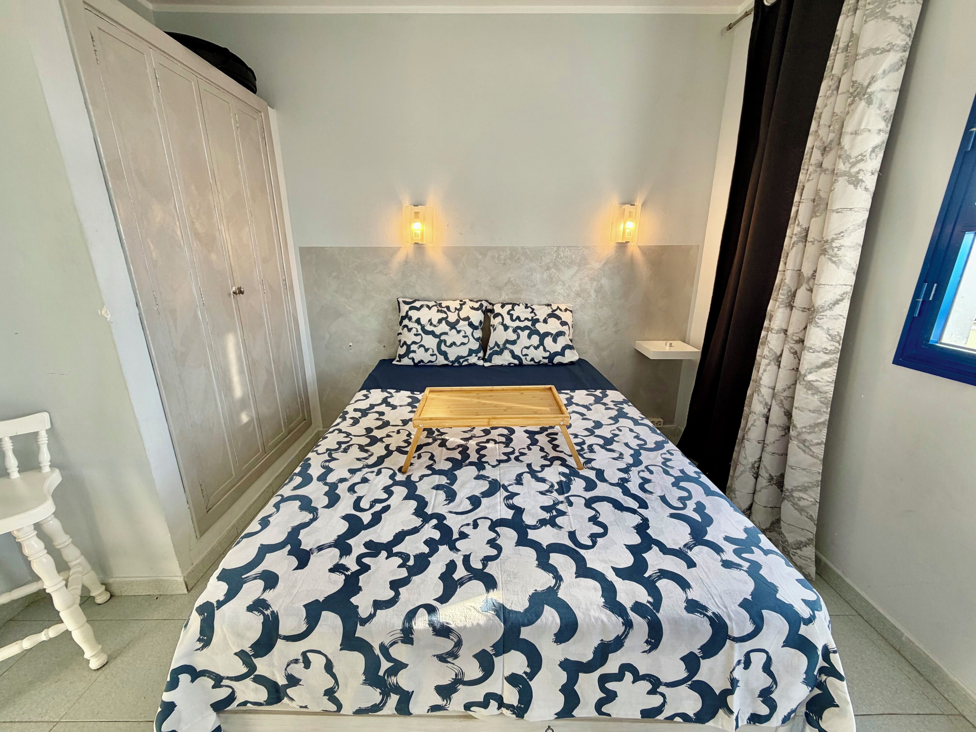 Ein Schlafzimmer mit einem Bett, zwei Wandleuchten, einem Nachttisch, einem Kleiderschrank und einem Fenster mit Vorhängen.