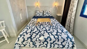 Ein Schlafzimmer mit einem Bett, zwei Wandleuchten, einem Nachttisch, einem Kleiderschrank und einem Fenster mit Vorhängen.
