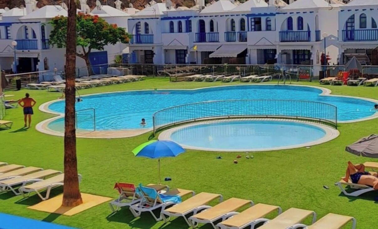 Ein Poolbereich mit Liegestühlen und Sonnenschirmen, umgeben von einem Gebäude mit blauen Balkonen.