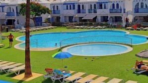 Ein Poolbereich mit Liegestühlen und Sonnenschirmen, umgeben von einem Gebäude mit blauen Balkonen.