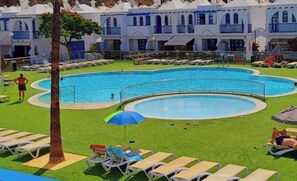 A pool area with lounge chairs and umbrellas, surrounded by a building with blue balconies.