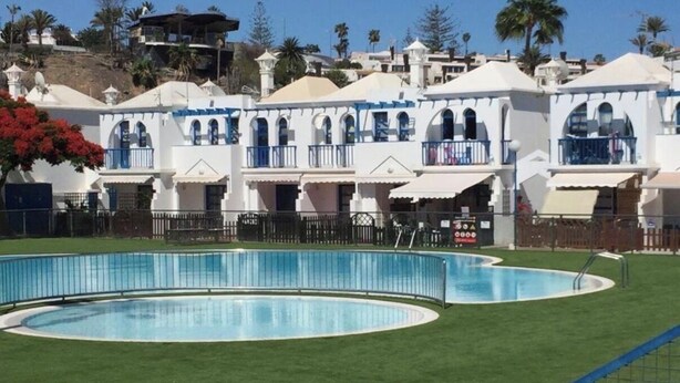 Ein Poolbereich mit einem kreisförmigen Pool und einem Gebäude im Hintergrund mit Balkonen.