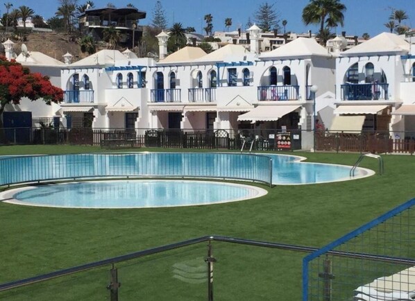 A pool area with a circular pool and a building with balconies in the background.