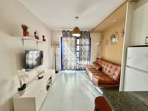 A modern kitchen with a flat-screen TV, a brown leather sofa, and a refrigerator.