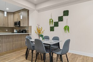 A modern kitchen with wooden cabinets, a microwave, and a dining area with a marble table and grey chairs. - 2BHK - Close to Downtown/Whyte Ave/UOFA (Edmonton)