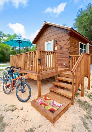 A wooden cabin with a deck, a bicycle, and a welcome mat.