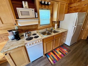 A compact kitchen with a stove, microwave, sink, and refrigerator.