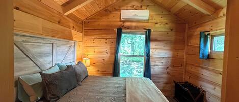 A wooden cabin room with a bed, a window, and a small table.