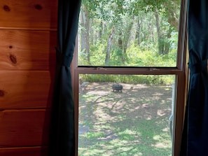 A window with a view of a forested area and a barbecue grill.