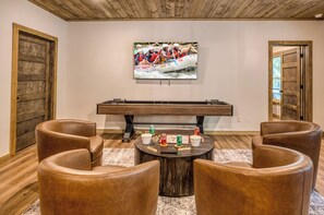 Ein gemütliches Zimmer mit Billardtisch, Ledersesseln und einem Fernseher, der eine Szene vom Rafting zeigt.