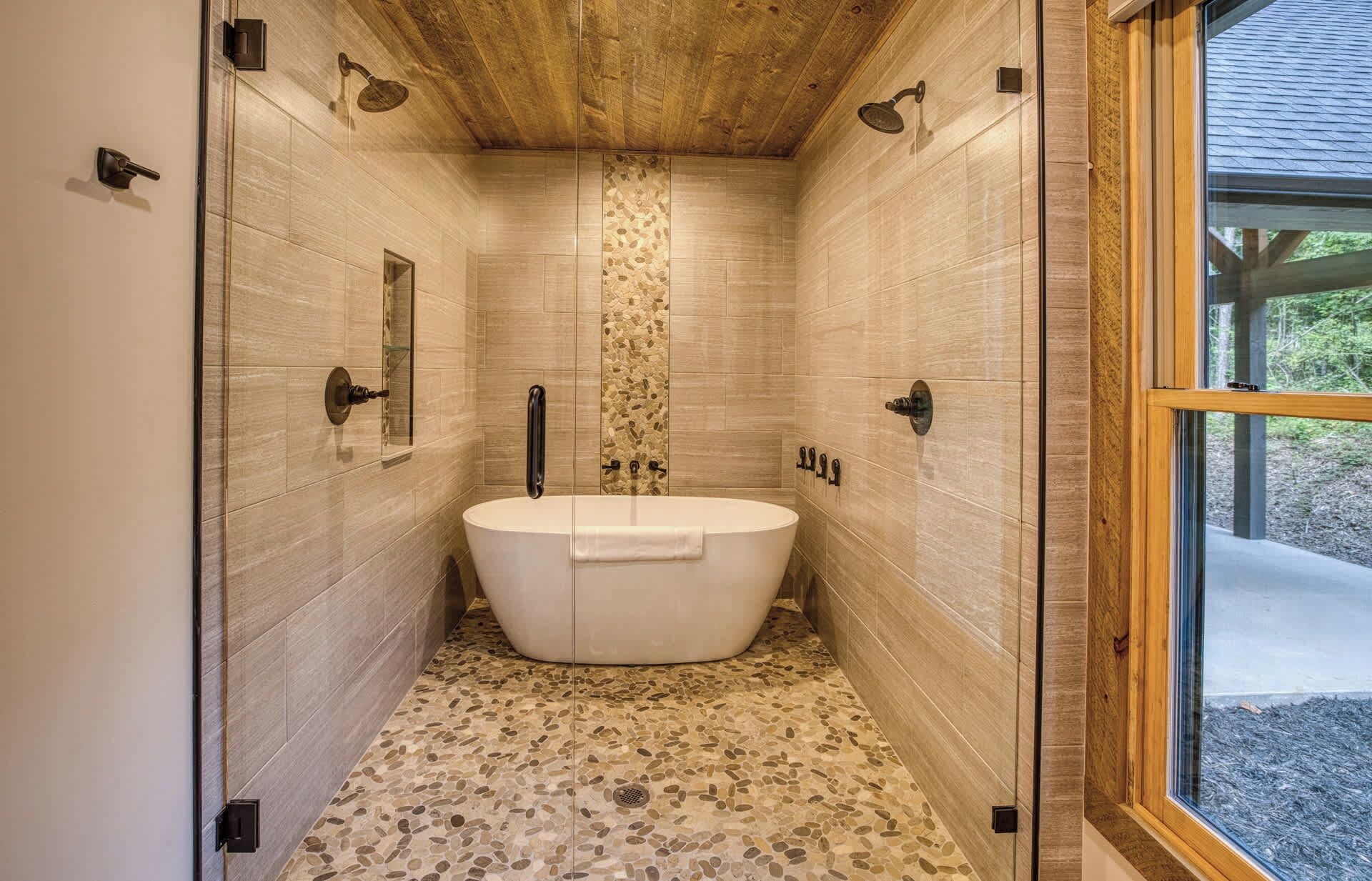 A modern bathroom with a freestanding bathtub, a shower area, and a large window providing a view of the outdoors.