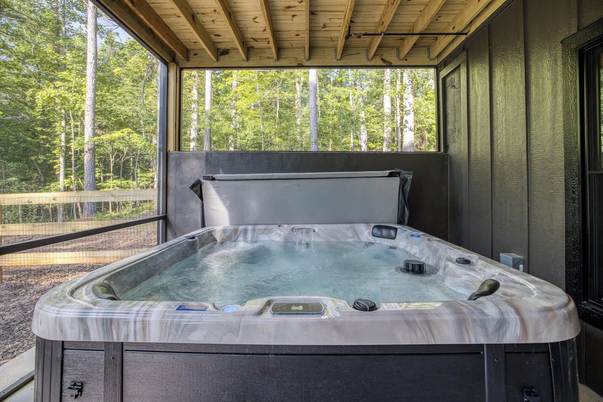 A hot tub with a wooden roof structure and a view of a forested area.