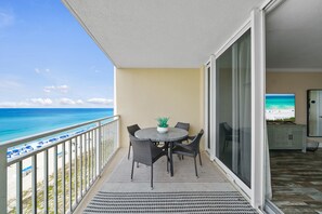 Ein Balkon mit Tisch und Stühlen, einem Blumentopf und Blick auf Strand und Meer.