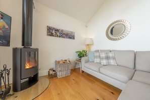 A living room with a wood-burning stove, a grey sofa, a mirror, and a painting on the wall. - Stylish Holiday Cottage In Rural Montgomery | Llety-Hiraeth (MONTGOMERY)