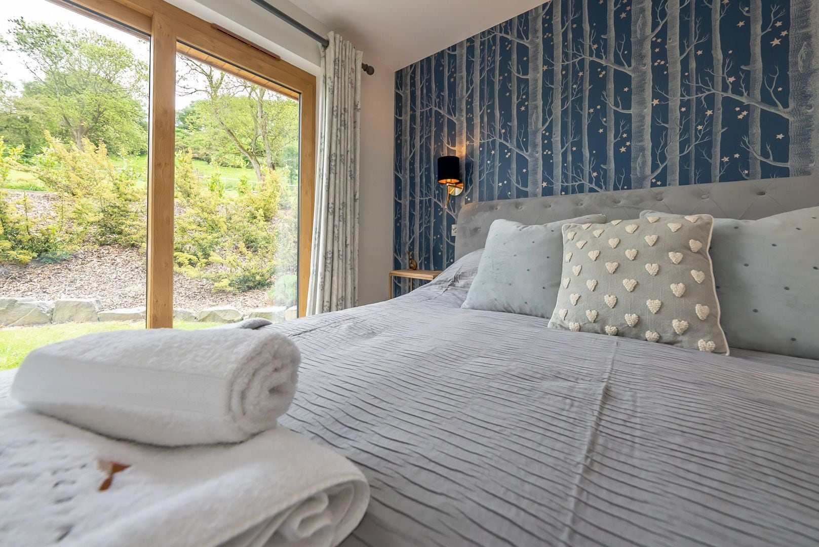 A bedroom with a large bed, a view of the outdoors, and a wall with a tree pattern.