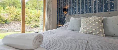 A bedroom with a large bed, a view of the outdoors, and a wall with a tree pattern.