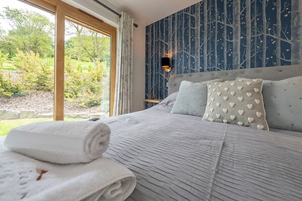 A bedroom with a large bed, a view of the outdoors, and a wall with a tree pattern.