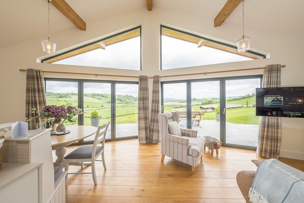 A spacious room with a large sliding glass door leading to a garden, a cozy seating area with a sofa and armchairs, and a flat-screen TV mounted on the wall.