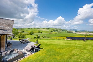 Eine Terrasse mit Sitzgelegenheiten im Freien und einem Whirlpool, mit Blick auf eine grüne Landschaft mit Solaranlagen.