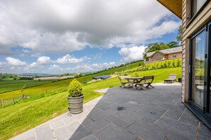Eine Terrasse mit Tisch und Stühlen, einem Blumentopf und Blick auf eine grüne Landschaft sowie entfernte Gebäude.