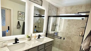 Une salle de bain moderne avec un grand miroir, deux lavabos, une douche et un porte-serviettes.
