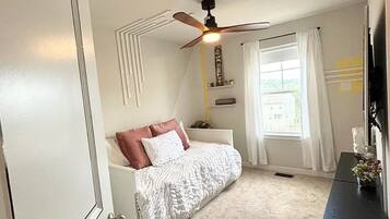 A bedroom with a bed, a ceiling fan, a window with curtains, and a dresser.