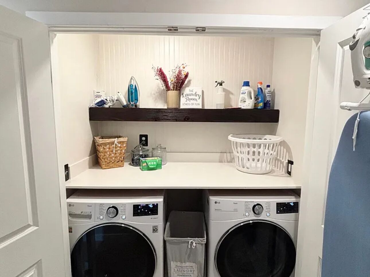 A laundry room with two washing machines, a shelf with laundry supplies, and a basket.