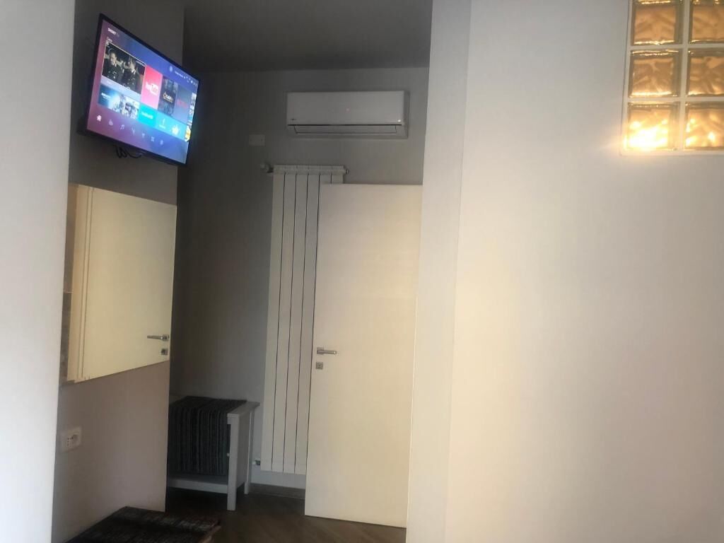 A room with a mounted television displaying a colorful interface, a radiator, a door, and a small table.