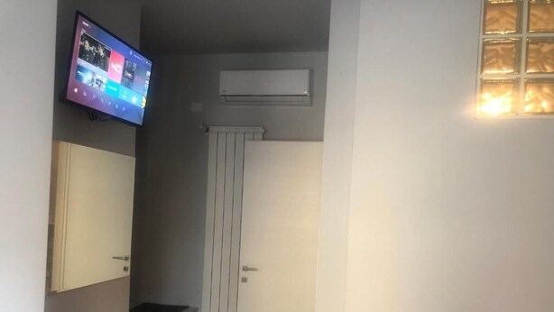 Ένα δωμάτιο με μια τηλεόραση τοποθετημένη στον τοίχο, η οποία προβάλλει μια πολύχρωμη διεπαφή, ένα καλοριφέρ, μια πόρτα και ένα μικρό τραπέζι.