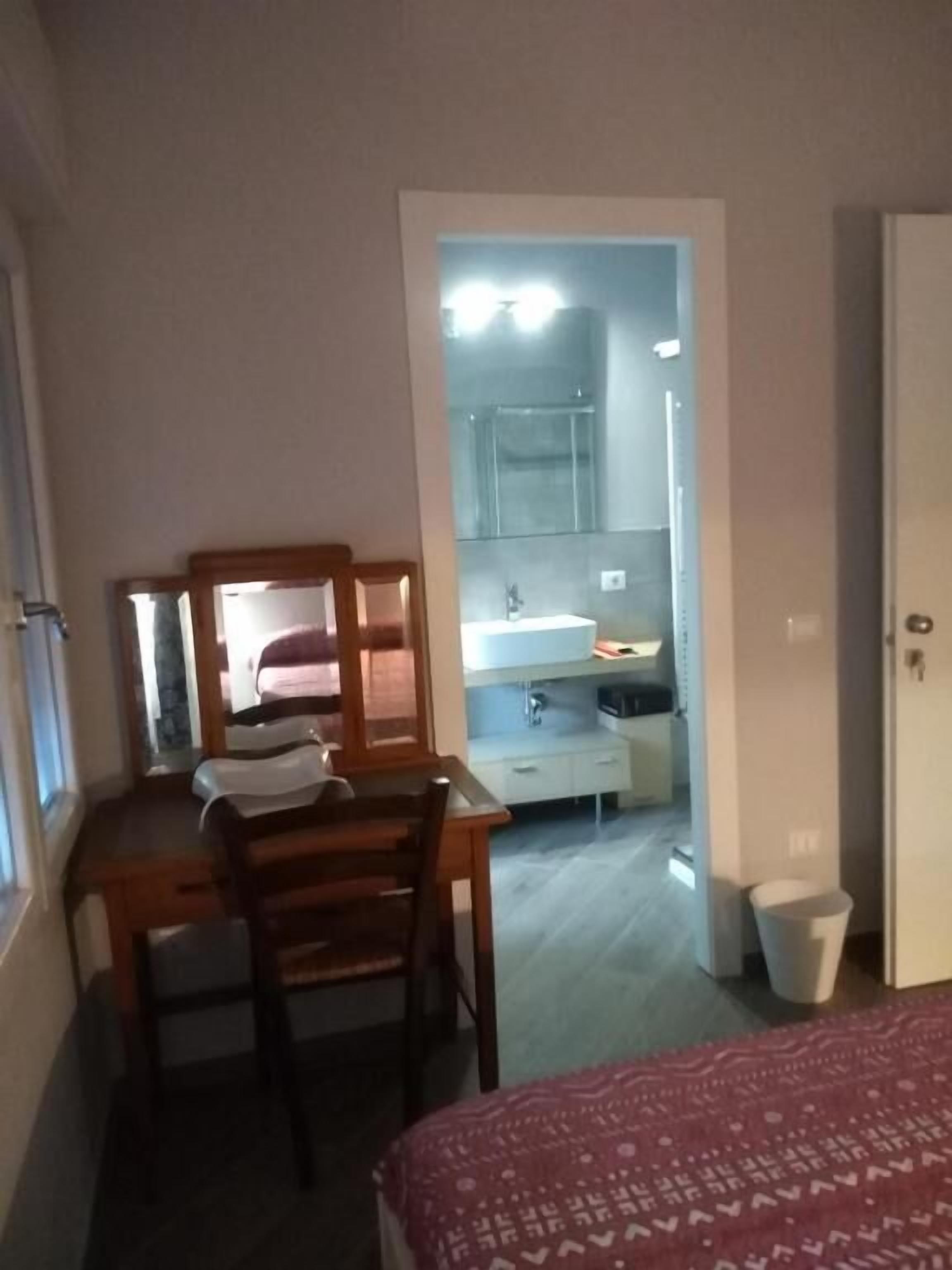A bedroom with a bed, a desk with a chair, a mirror, and a door leading to a bathroom.