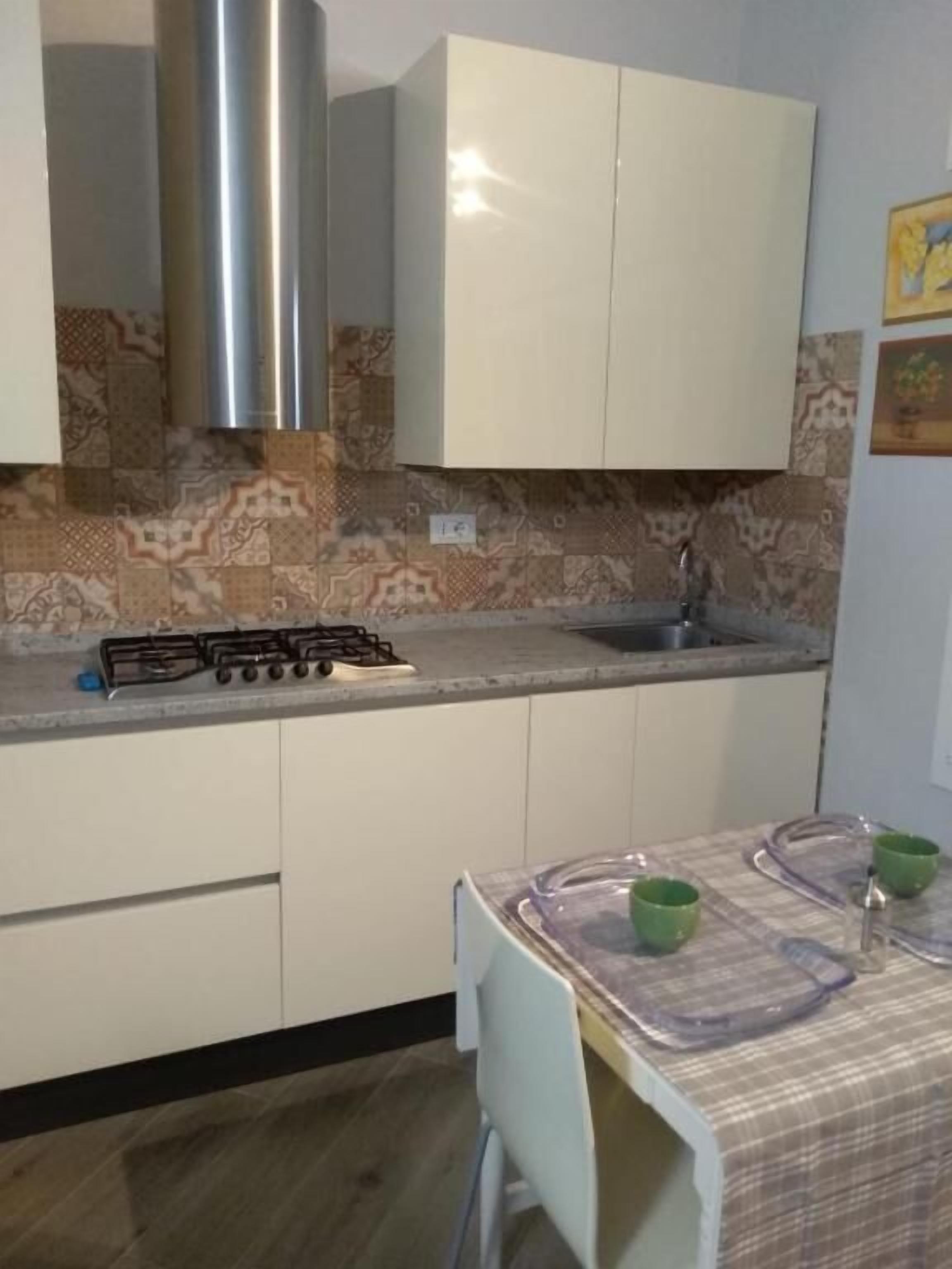 Une cuisine de taille réduite, dotée d’une cuisinière à gaz, de meubles blancs et d’un crédence décorée.