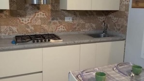 Ett kompakt kök med en gasspis, vita skåp och en mönstrad väggbeklädnad bakom arbetsbänken.