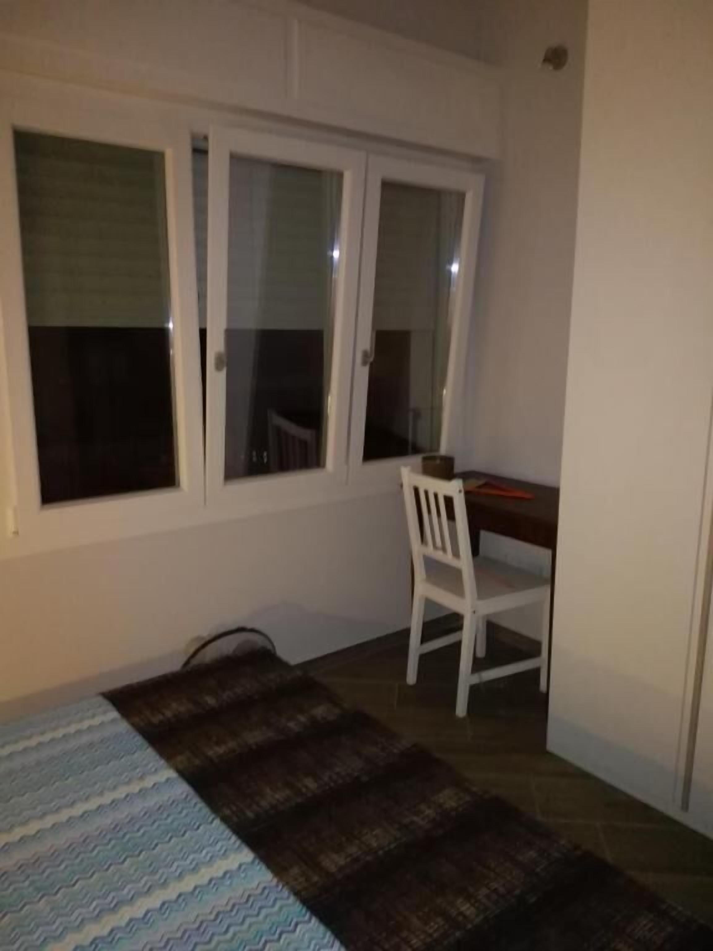 A room with a bed, a desk, and a chair. There is a window with blinds.