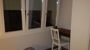 Ένα δωμάτιο με ένα κρεβάτι, ένα γραφείο και μια καρέκλα. Υπάρχει ένα παράθυρο με περσίδες.