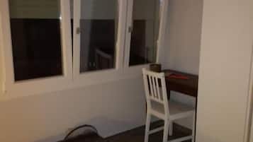 A room with a bed, a desk, and a chair. There is a window with blinds.