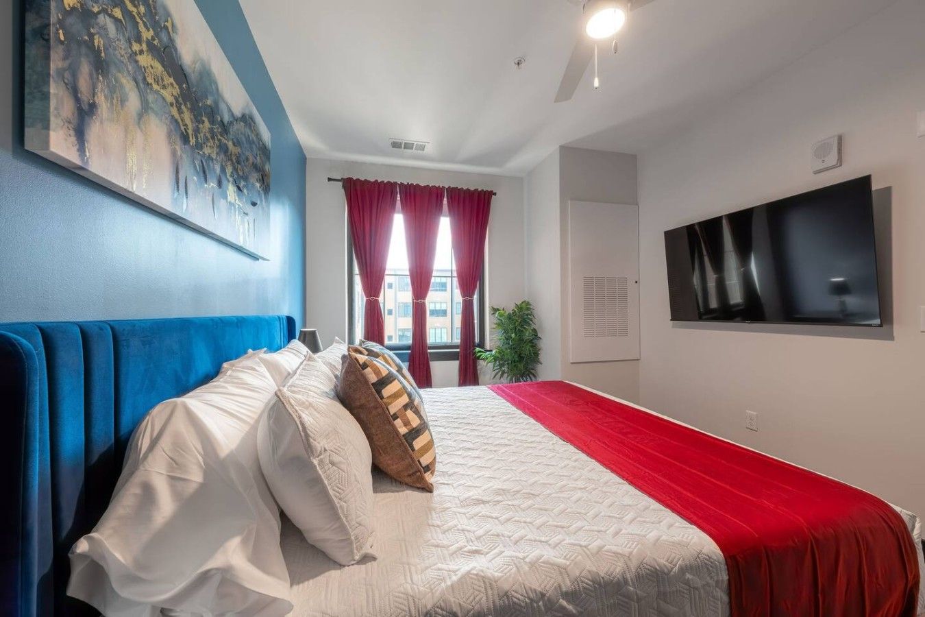 A hotel room with a bed, a TV, and a painting on the wall.