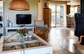 A living room with a television, a glass table with rocks and a plant, a wooden chair, and a large woven light fixture. - Gorgeous home in Thisted with sauna (Thisted)