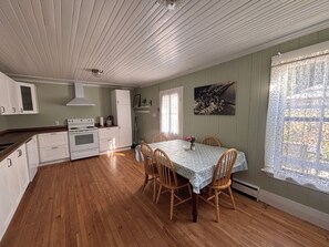 A kitchen with white cabinets, a stove, and a dining table with chairs. - The “Dining Room” A 5-bedroom cottage perfect for large families. Clyffe House (Port Sydney)