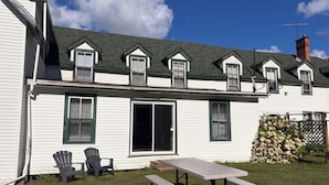 A two-story house with a covered patio area, a large sliding glass door, and a chimney. - The “Dining Room”: A charming 5-bedroom cottage perfect for large families (Port Sydney)
