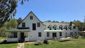 A white two-story house with a covered porch and a stone pathway leading to the entrance. - The “Dining Room”: A charming 5-bedroom cottage perfect for large families (Port Sydney)