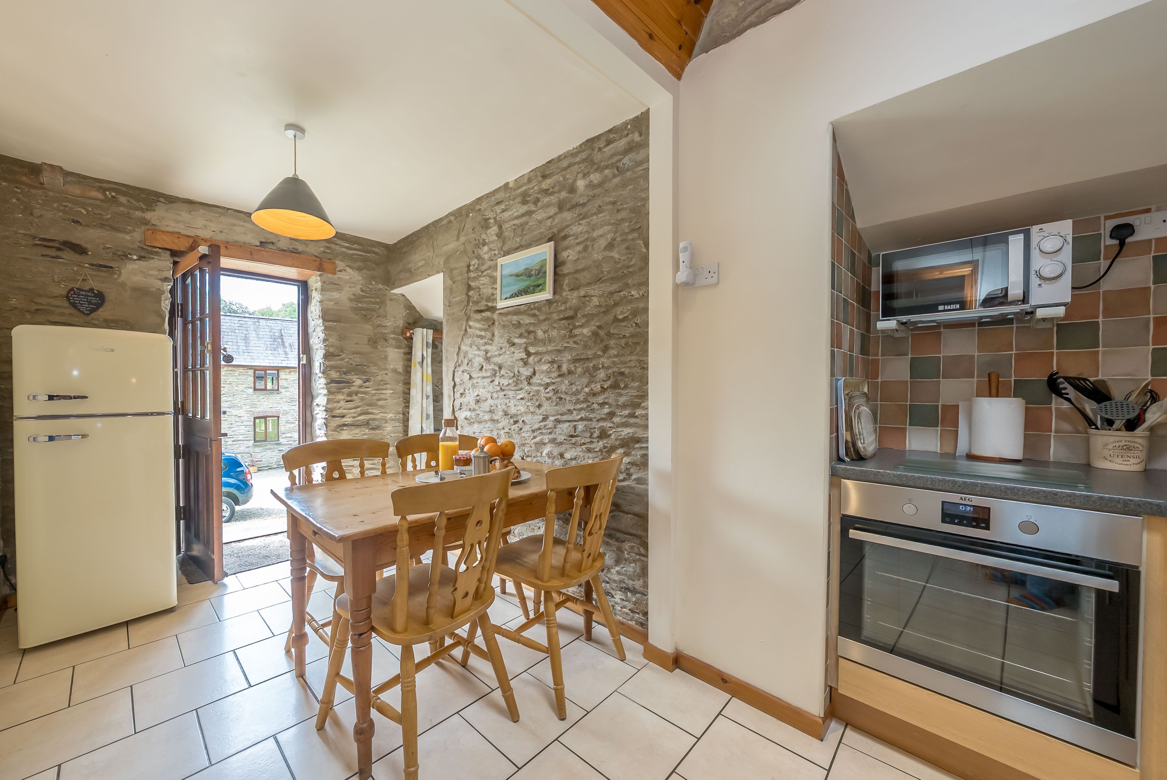 A kitchen with a stone wall, a dining table with chairs, a refrigerator, a stove, and a microwave.