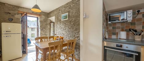 Una cocina con pared de piedra, una mesa de comedor con sillas, un refrigerador, una estufa y un microondas.