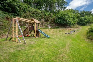 Ein Spielplatz mit einer Holzwentil und Rutsche, umgeben von Gras und Bäumen.