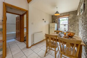 Eine gemütliche Küche mit einem Holztisch, Stühlen, einem Kühlschrank und einem Fenster mit Blick auf ein Steinhaus.