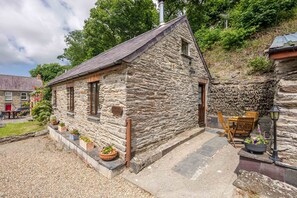 Ein Steinhäuschen mit geneigtem Dach, einer kleinen Veranda mit Sitzgelegenheit und einem Schild, das es als 'Horse Cottage' kennzeichnet.